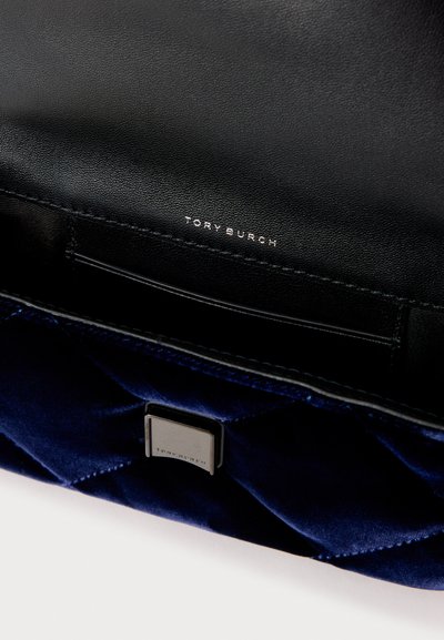 Mala de veludo azul-marinho acolchoada com interior em pele preta. Apresenta uma etiqueta com o logótipo "Tory Burch" em prata e um detalhe metálico no exterior.