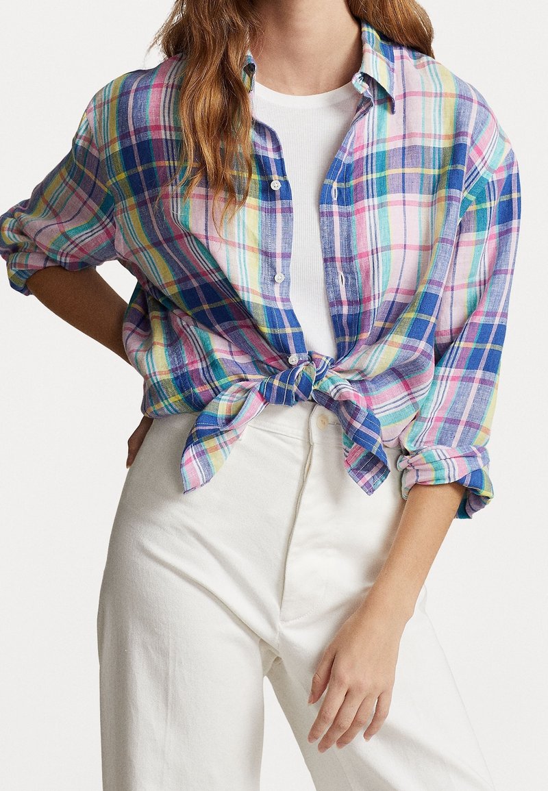 Chemise à carreaux dans des tons multicolores de bleu, rose et vert, avec un design à boutons et un détail noué à l'avant. Portée sur un haut blanc.