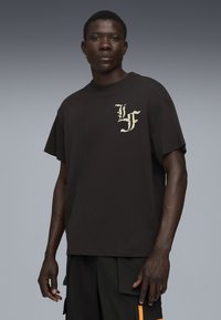 Sort kortærmet T-shirt med et hvidt grafisk design på venstre brystområde. Fremstillet af bomuld med en løs pasform.