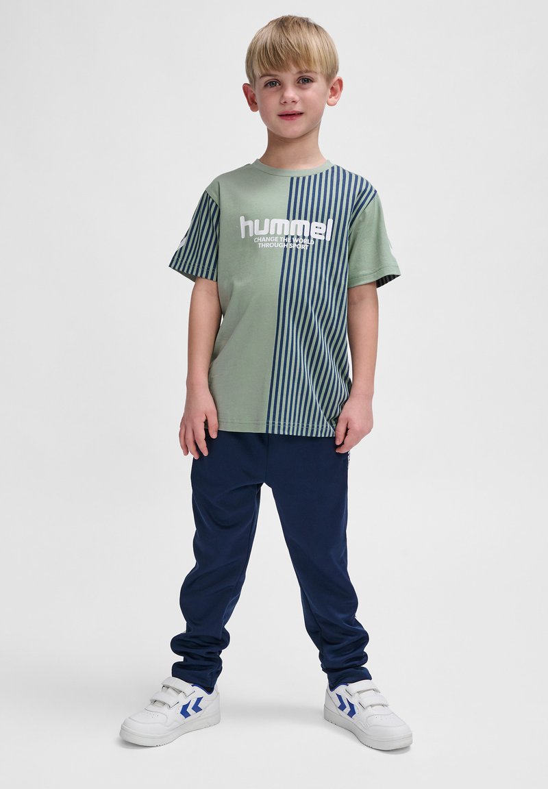 T-shirt rayé vert et marine avec logo blanc, assorti à un pantalon marine et des chaussures de sport blanches avec des accents bleus.
