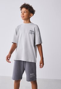 Lichtgrijs katoenen T-shirt met korte mouwen en een logo op de borst, gecombineerd met donkergrijze katoenen shorts met zijzakken en logodetail.