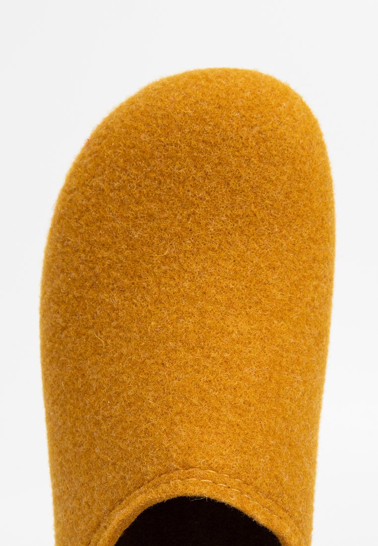 Nahaufnahme eines senfgelben Wollfilzschlittschuhs mit abgerundetem Zeh und genähtem Rand auf weißem Hintergrund.