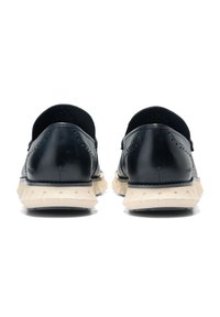 Läderskor med en slät svart ovandel, dekorativa perforeringar och en kontrasterande beige gummisula med texturerat mönster.