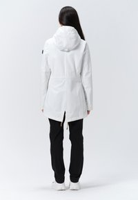 Weiße wasserdichte Jacke mit Kapuze, tailliertes Mittellängen-Design und Kordelzug in der Taille. Kombiniert mit schwarzen Hosen und weißen Sneakers.