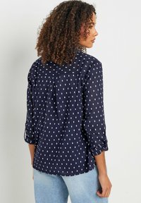Camisa de color navy con patrones rectangulares blancos, mangas largas arremangadas, detalle de pliegue en la parte posterior y un ajuste relajado. La tela parece ligera y transpirable.
