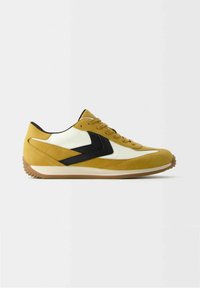 Retro-stil sneakers i gul mocka och vit läder, med svarta accenter, rund tå och en texturerad gummisula.