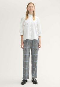 Witte lange mouwen blouse gecombineerd met grijs geruite broek met blauwe strepen; model draagt zwarte platform schoenen.