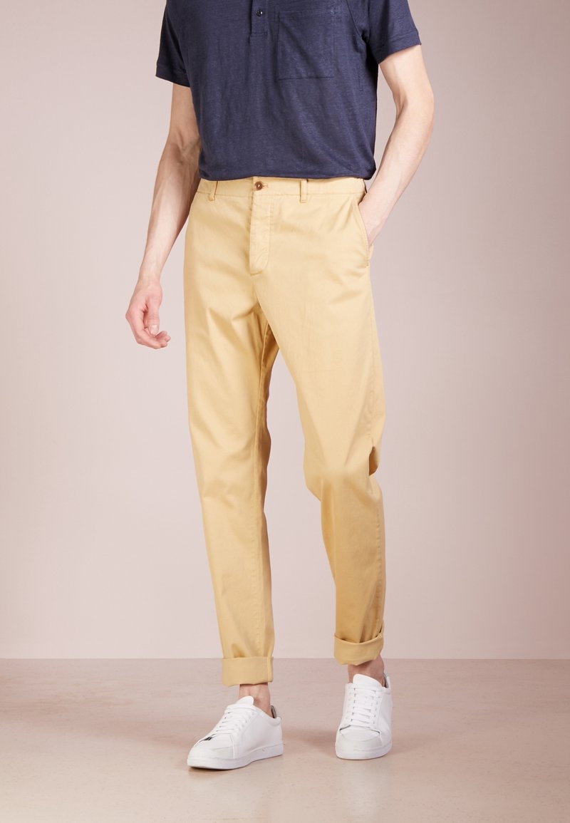 Light yellow, cotton chinos with a relaxed fit, rolled cuffs, and a front button closure, paired with white sneakers and a dark polo shirt.