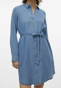 Abito camicia in denim di colore azzurro chiaro, con chiusura a bottoni davanti, colletto, maniche lunghe e dettaglio vita annodata. Tessuto morbido con una vestibilità leggermente rilassata.