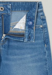 Modré džíny z denimu se zipem, knoflíkovým zapínáním a viditelným prošitím. Mezi zvláštními rysy se nachází texturovaná látka a zesílené kapsy.