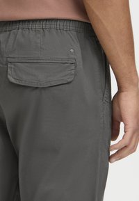 Gray elastic waistband pants with a back pocket. The fabric has a smooth texture, and there's a small branded button near the pocket.