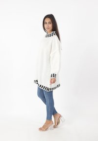 Hvid oversized sweater med sorte stribede detaljer ved kraven og kanten, parret med blå skinny jeans og klare blokhælede sandaler.