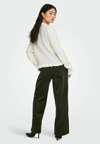 Pullover chiaro in crema con orlo garnito da volant, abbinato a pantaloni in velluto a coste verde scuro a gamba larga e tacchi a punta nera.