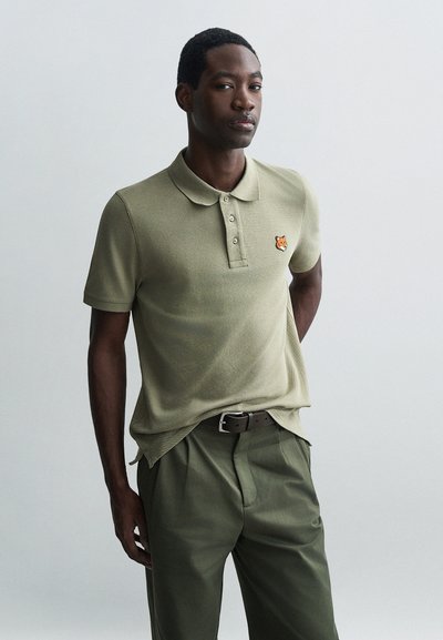 Polo olive avec un tissu texturé, patte de boutonnage à trois boutons et un logo de renard brodé sur la poitrine gauche. Associé à un pantalon assorti.