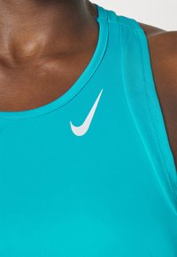 Débardeur de sport turquoise avec un col arrondi, arborant un logo Nike blanc sur le côté gauche, fabriqué en tissu lisse et extensible.