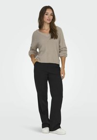 Lichtbeige, losse trui met een V-hals en opgerolde mouwen, gecombineerd met zwarte, wijde broekspijpen en witte sneakers.