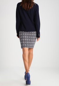 Blazer blu navy abbinato a una gonna a matita a fantasia bianca e nera. Décolleté blu scuro, tessuto liscio, silhouette aderente e dettagli hardware accurati.