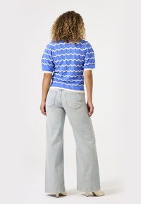 Top de mangas cortas con patrón ondulado en azul, combinado con unos jeans de pierna ancha en azul claro. Arriba tiene un acabado acanalado texturizado, mientras que los jeans tienen un acabado liso.