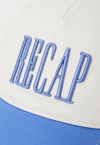 White cap with a blue curved brim featuring raised blue embroidery spelling "RECAP." The fabric is textured, with visible stitching detail.