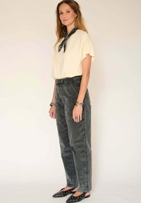 Haut jaune clair à manches courtes, pantalon taille haute gris charbon et chaussures noires à enfiler avec des accents décoratifs. Bracelets en argent et écharpe noire.