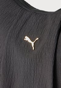 Μαύρο υφασμάτινο υλικό με μικρό, γυαλιστερό χρυσό λογότυπο Puma κοντά σε μαύρο φερμουάρ.