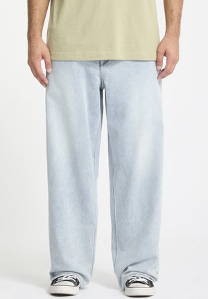 Light blue denim jeans with a loose fit, straight legs, and a faded finish. Worn with black sneakers featuring white accents.