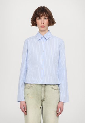 Hellblaues, kurzes Button-Up-Hemd mit vertikalen weißen Streifen, Punktkragen und langen Ärmeln, kombiniert mit lässigen, hellgrünen Jeans.
