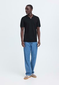 Polo noir à manches courtes, associé à un jean large bleu clair et des baskets grises à rayures blanches. Design simple et épuré.