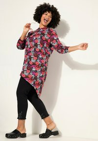Tunika a maniche lunghe con un motivo di labbra colorate, abbinata a leggings neri con orli borchiati e zoccoli neri. Design vivace e giocoso.