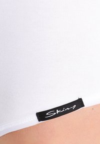 Witte katoenen stretchshorts met een gladde textuur en een zwart "Skiny" label aan de zoom, met een strakke pasvorm en ribbelstof.
