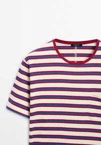 Puuvillainen t-paita, jossa on vaakaraitoja punaisena, sinisenä ja beigenä. Siinä on pyöreä kaulus ja rintatasku, sekä pehmeä pinta.