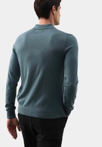 Pull bleu clair à manches longues avec un ourlet et un col côtelés, fabriqué en matériau tricoté doux, porté sur un jean foncé.