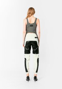 Top ajustado gris, pantalones de cuero blancos y negros con bolsillos laterales y cintura elástica, combinados con zapatos de tacón negros.