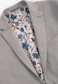 Blazer grigio chiaro con esterno in tessuto liscio; fodera floreale a motivo nei toni del blu, verde e oro su sfondo crema.