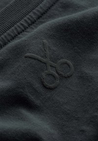 Zwarte stof met een gestructureerde afwerking met een donker geborduurd schaarlogo. Het materiaal lijkt zacht en flexibel bij een close-up weergave.