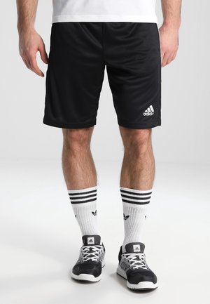 Czarne sportowe spodenki z elastycznym paskiem w talii, z białym logo Adidas. Nosi się je z białymi i czarnymi skarpetami w paski oraz czarnymi trampkami.