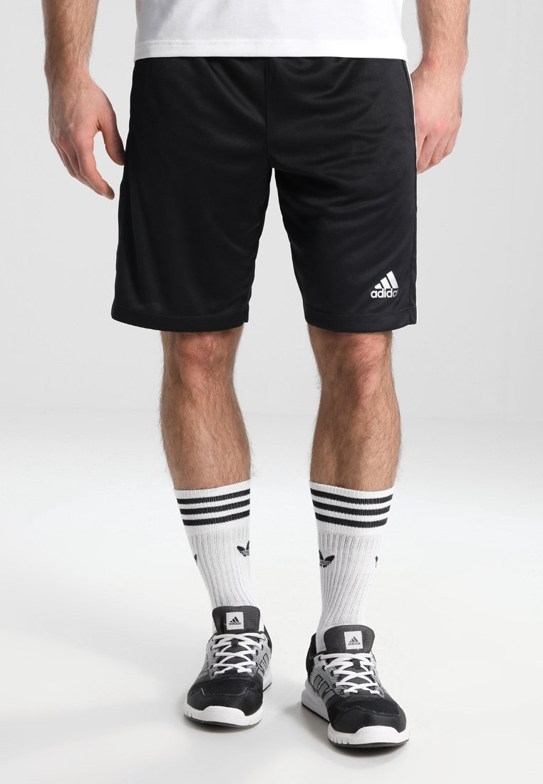 Shorts de sport noirs avec une ceinture élastique, portant le logo Adidas blanc. Portés avec des chaussettes blanches à rayures noires et des baskets noires.
