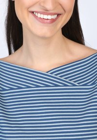 Gestreifter Stoff in Blau und Hellblau mit einem Überkreuz-Ausschnitt, der eine glatte Textur zeigt. Nahaufnahme eines lächelnden Gesichts.