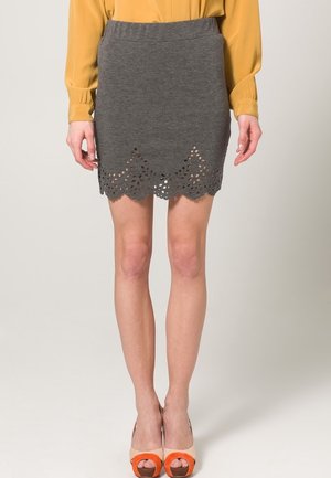 Jupe en tricot grise avec un ourlet à volants et un motif floral découpé. Associée à un haut moutarde et des sandales à plateforme bicolores.
