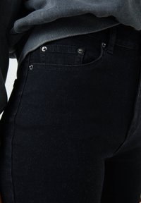 Gros plan sur une personne portant un jean bleu foncé et un pull gris rentré, mettant en valeur les détails de la poche et de la taille du jean.