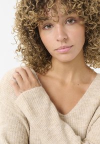 Beige, weicher Strickpullover mit tiefem V-Ausschnitt und gerippter Textur. Lange Ärmel, leicht oversized Passform, die fusselige Fasern zur Geltung bringt.