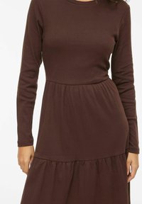 Robe marron à manches longues en tissu côtelé, avec un corsage ajusté et une jupe à volants froncée pour une coupe décontractée.