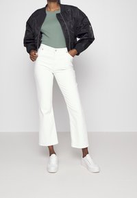 Musta pommitakki, vihreä t-paita, valkoiset leveälahkeiset farkut ja valkoiset tennarit. Takissa on kiiltävä pinta; housut ovat farkkua ja niiden leikkaus on levenevä.