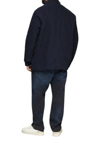 Granatowa bawełniana kurtka o luźnym kroju, z kołnierzem i bocznymi kieszeniami, w zestawie z ciemnoniebieskimi dżinsami i białymi trampkami.