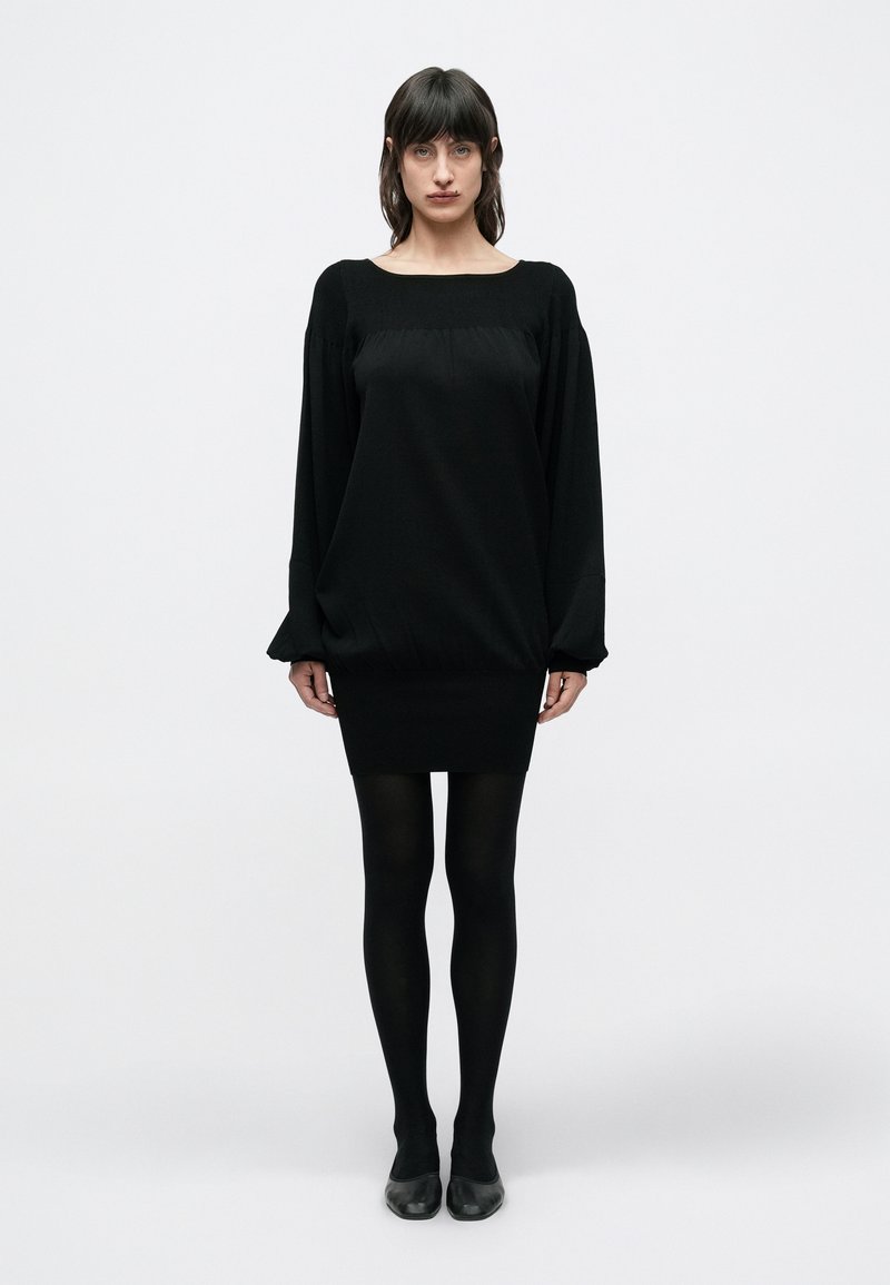 Μαύρο φόρεμα με τετράγωνη λαιμόκοψη, φαρδιά κορυφή και εφαρμοστή φούστα. Διαθέτει μακριά, σούρες μανίκια και απαλή υφή. Φοριέται με μαύρες καλσόν.