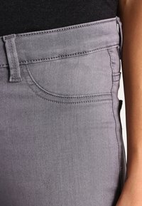 Jeans de mezclilla gris con un diseño ajustado, cintura de altura media, textura sutil y bolsillos delanteros. Detalles de costura a lo largo de las costuras.