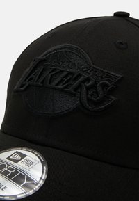 Juodas beisbolo kepuraitė, pagaminta iš audinio, su iškilniu Los Andželo Lakers logotipu. Dizainas apima išlenktą skydelį ir New Era lipduką.