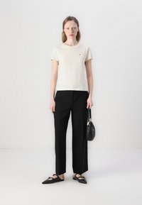 T-shirt a maniche corte color crema chiaro, pantaloni neri a gamba larga, scarpe nere basse con punta affusolata e una piccola borsa nera. Design semplice.