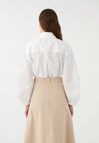 Camicia bianca con maniche a sbuffo, abbinata a una gonna beige alta in vita. Texture morbide e un design pulito e minimalista.