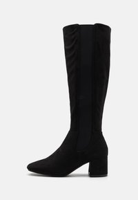 Botte noire en daim montant jusqu'au genou avec un bout pointu, un talon bloc, et des panneaux latéraux élastiques pour faciliter l'enfilage. Texture lisse sans motifs visibles.